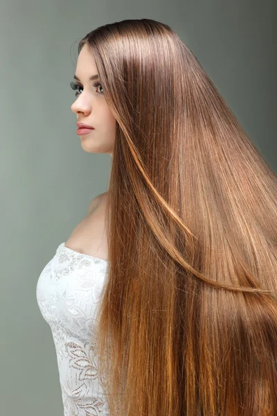 Retrato de chica hermosa con pelos largos, sobre un fondo gris, emociones, cosméticos — Foto de Stock