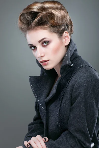 Portrait of elegant young woman in a grey overcoat on a grey background — Stock Photo, Image