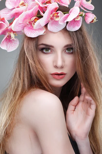 Красива дівчина, ізольована на світлому - сірому тлі з рожевими орхідеями в волоссі, емоціях, косметиці — стокове фото