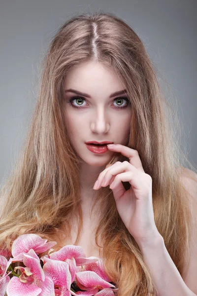 Hermosa chica, aislada sobre un fondo gris claro con orquídeas rosadas, emociones, cosméticos — Foto de Stock