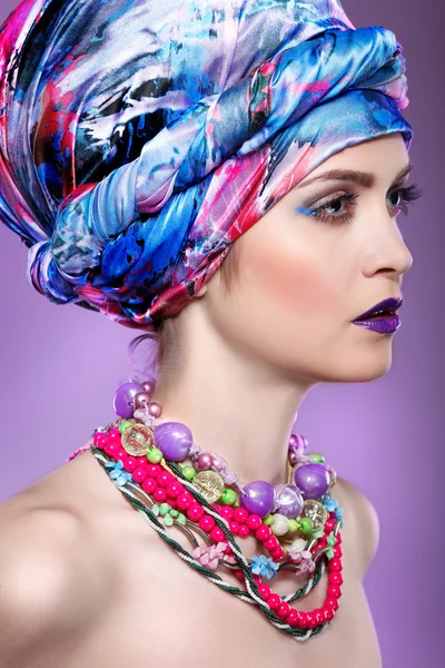 Een foto van een mooi meisje in een hoofd-jurk van de gekleurde stof, op een violette achtergrond, glamour — Stockfoto