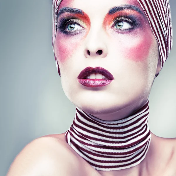 Портрет девушки с ярким театральным макияжем с полосатым шарфом на голове — стоковое фото