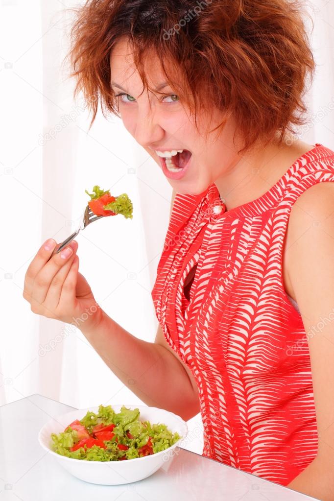 Angry young girl eating tasty salad