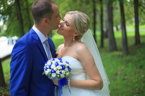 Pareja de boda recién casados novia y novio en el amor en el día de la boda al aire libre. Feliz pareja amorosa en el día de la novia abrazando. recién casados con flores de ramo. Relación. Sonriente esposa y marido beso — Foto de Stock