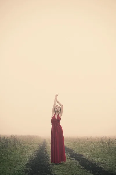 Girl in a red dress walking through field — Stock Photo, Image