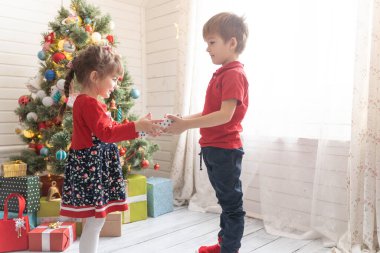 Oğlan, parlak güneşli bir odada bir kıza Noel hediyesi verir.
