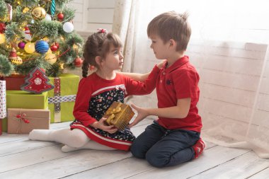 Oğlan, parlak güneşli bir odada bir kıza Noel hediyesi verir.