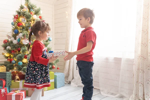 Niño da un regalo de Navidad a una chica en una habitación soleada brillante Imagen De Stock