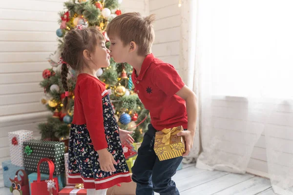 Niño da un regalo de Navidad a una chica en una habitación soleada brillante Imágenes De Stock Sin Royalties Gratis