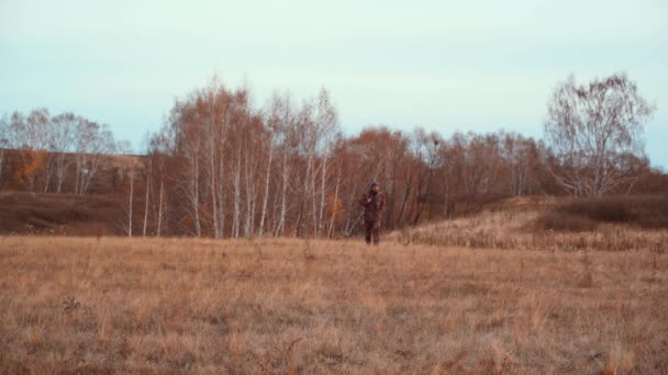 Een jager met een jachtgeweer loopt door een herfstveld. — Stockvideo