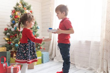 Oğlan, parlak güneşli bir odada bir kıza Noel hediyesi verir.
