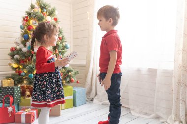 Oğlan, parlak güneşli bir odada bir kıza Noel hediyesi verir.