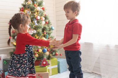 Oğlan, parlak güneşli bir odada bir kıza Noel hediyesi verir.