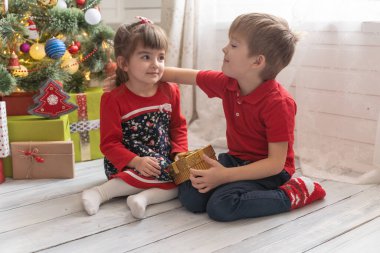 Oğlan, parlak güneşli bir odada bir kıza Noel hediyesi verir.