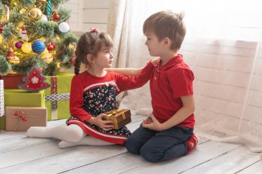 Oğlan, parlak güneşli bir odada bir kıza Noel hediyesi verir.