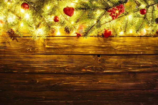 Rozmazané vánoční pozadí, s jedlovými větvemi, víla světla a vánoční ozdoby na dřevěné desce — Stock fotografie