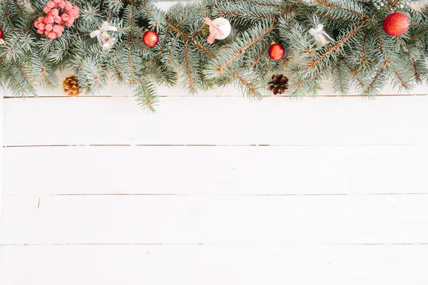 Abeto de Navidad sobre fondo de madera. Fondo borroso de Navidad, con ramas de abeto, luces de hadas y decoraciones navideñas en tablón de madera blanca Imagen De Stock