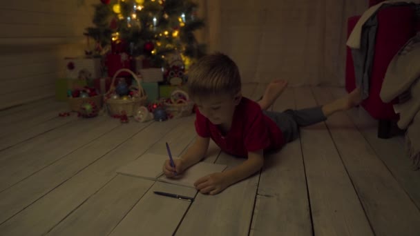 子供の男の子はサンタに手紙を書き、クリスマスのために望むものを書きます — ストック動画
