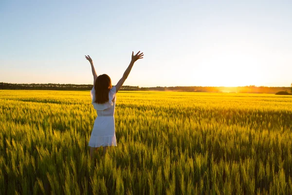 Beautiful caucasian woman in white dress jumping up with raised hands outdoor. Field with yellow wheat around — Stock Photo, Image