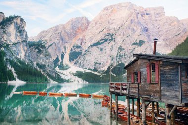 Kırmızı elbiseli ve şapkalı bir kız gölün ortasında teknelere ve dağlara tepeden bakan tek başına duruyor. Göl dağları yansıtır. Bries Gölü. Lago di Bries 