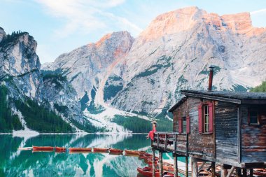 Kırmızı elbiseli ve şapkalı bir kız gölün ortasında teknelere ve dağlara tepeden bakan tek başına duruyor. Göl dağları yansıtır. Bries Gölü. Lago di Bries 