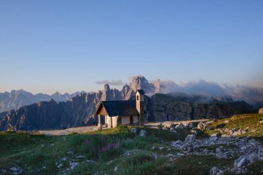 Three Peaks Tre Cime di Lavaredo Massive Rock, Sexten Dolomites, South Tyrol, Dolomite Alps, İtalya 'ya sabah yürüyüşü. Dağlarda küçük bir kilise. Kilisenin yanında büyük taşlı yeşil çimenler. 