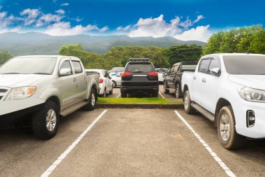 Ağaçlı, beyaz bulutlu, mavi gökyüzü ve dağ zeminli büyük asfalt otoparka park edilmiş bir araba. Açık hava otoparkı doğa ve yeşil seyahat ulaşım konsepti ortamı