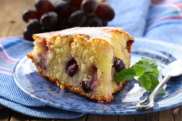 Spons cake met rode druiven op een plaat — Stockfoto