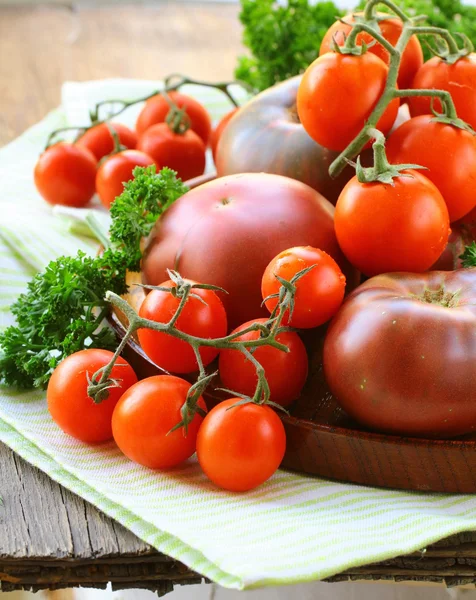 Different varieties of tomatoes on wooden plate — Stock Photo, Image