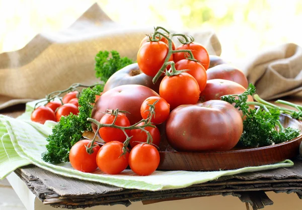 Different varieties of tomatoes on wooden plate — Stock Photo, Image