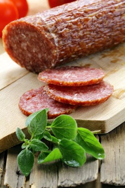 Skivat kött korv salami på träplatta med gröna örter — Stockfoto