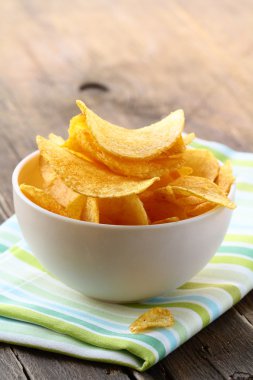 ahşap bir masa üzerinde beyaz bir kase içinde patates cipsi