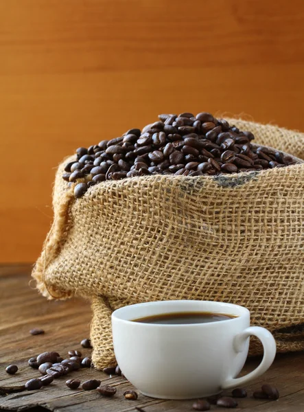 Linen bag of coffee beans and a cup of espresso on a wooden table — Stock Photo, Image