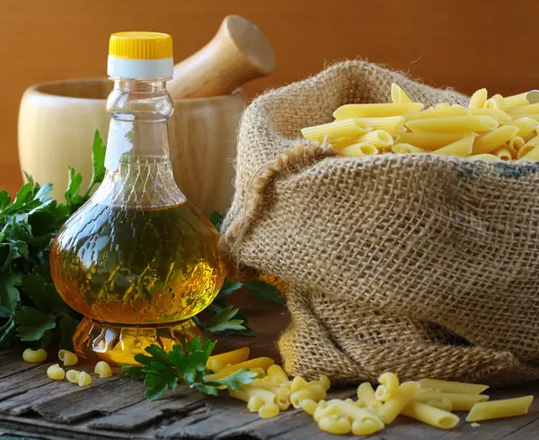 Linen bag of pasta (penne) and a bottle of oil on wooden table — Stock Photo, Image