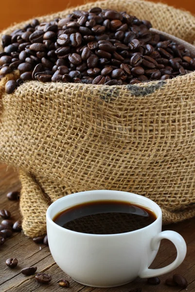 Linen bag of coffee beans and a cup of espresso on a wooden table — Stock Photo, Image