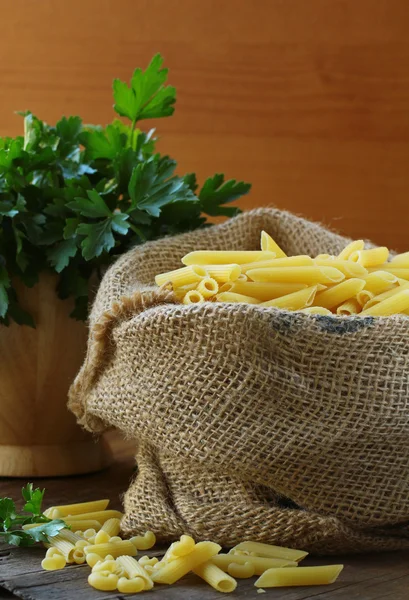 Linen bag of pasta (penne) on a wooden table — Stock Photo, Image