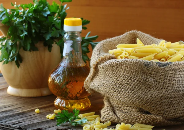 Sacchetto di lino di pasta (penne) e una bottiglia di olio sul tavolo di legno — Foto Stock