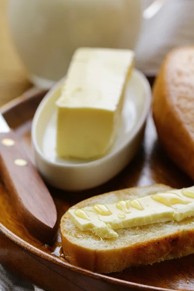 Масло, буханка белого хлеба и молоко на деревянной тарелке — стоковое фото
