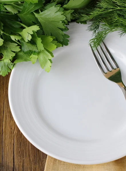 Placa blanca vacía con tenedor sobre mesa de madera con perejil y eneldo — Foto de Stock