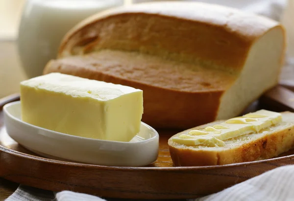 Масло, буханка белого хлеба и молоко на деревянной тарелке — стоковое фото