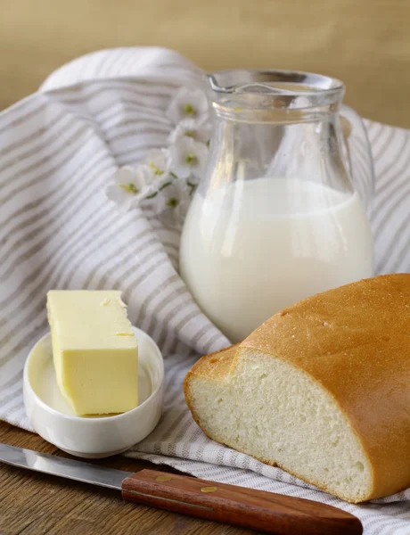 Масло, буханка белого хлеба и молоко на деревянном столе — стоковое фото