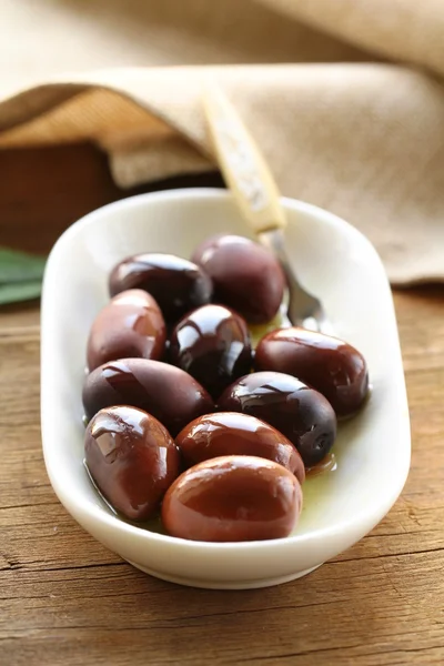 Natural organic olives in a white bowl, a bottle of oil in the background — Stock Photo, Image