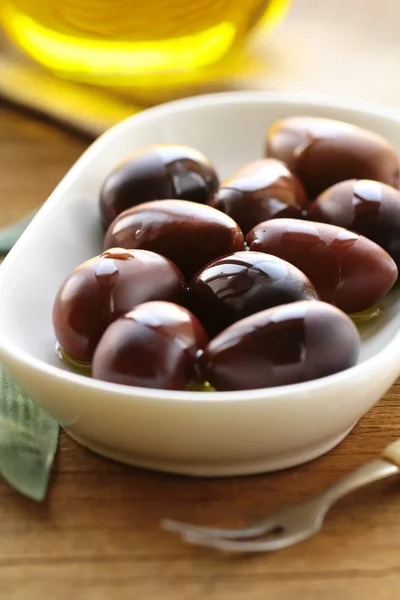 Natural organic olives in a white bowl, a bottle of oil in the background — Stock Photo, Image