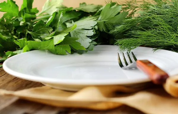 Placa blanca vacía con tenedor sobre mesa de madera con perejil y eneldo —  Fotos de Stock