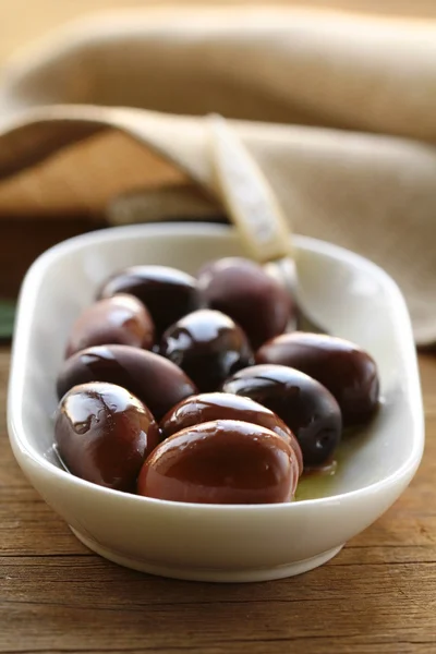 Natural organic olives in a white bowl, a bottle of oil in the background — Stock Photo, Image