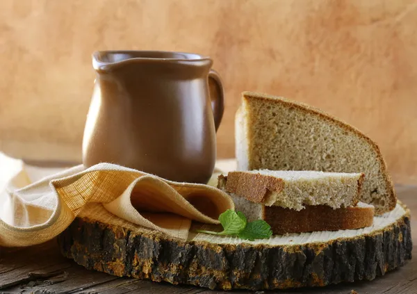 Ceramic jug with milk and a loaf rye black bread, on a wooden table , rustic style — Stock Photo, Image