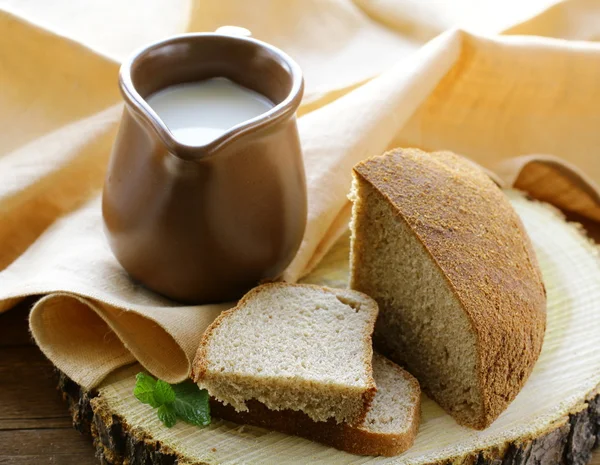 Pot en céramique avec lait et pain de seigle noir, sur une table en bois, style rustique — Photo