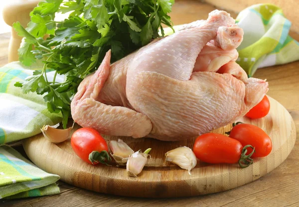 Färsk rå kyckling på en skärbräda med grönsaker och örter — Stockfoto