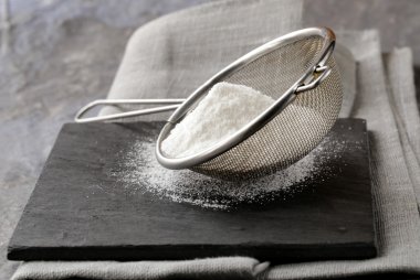 gri bir arka plan üzerinde metal bir süzgeç içinde toz şeker