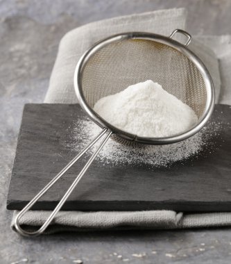 gri bir arka plan üzerinde metal bir süzgeç içinde toz şeker